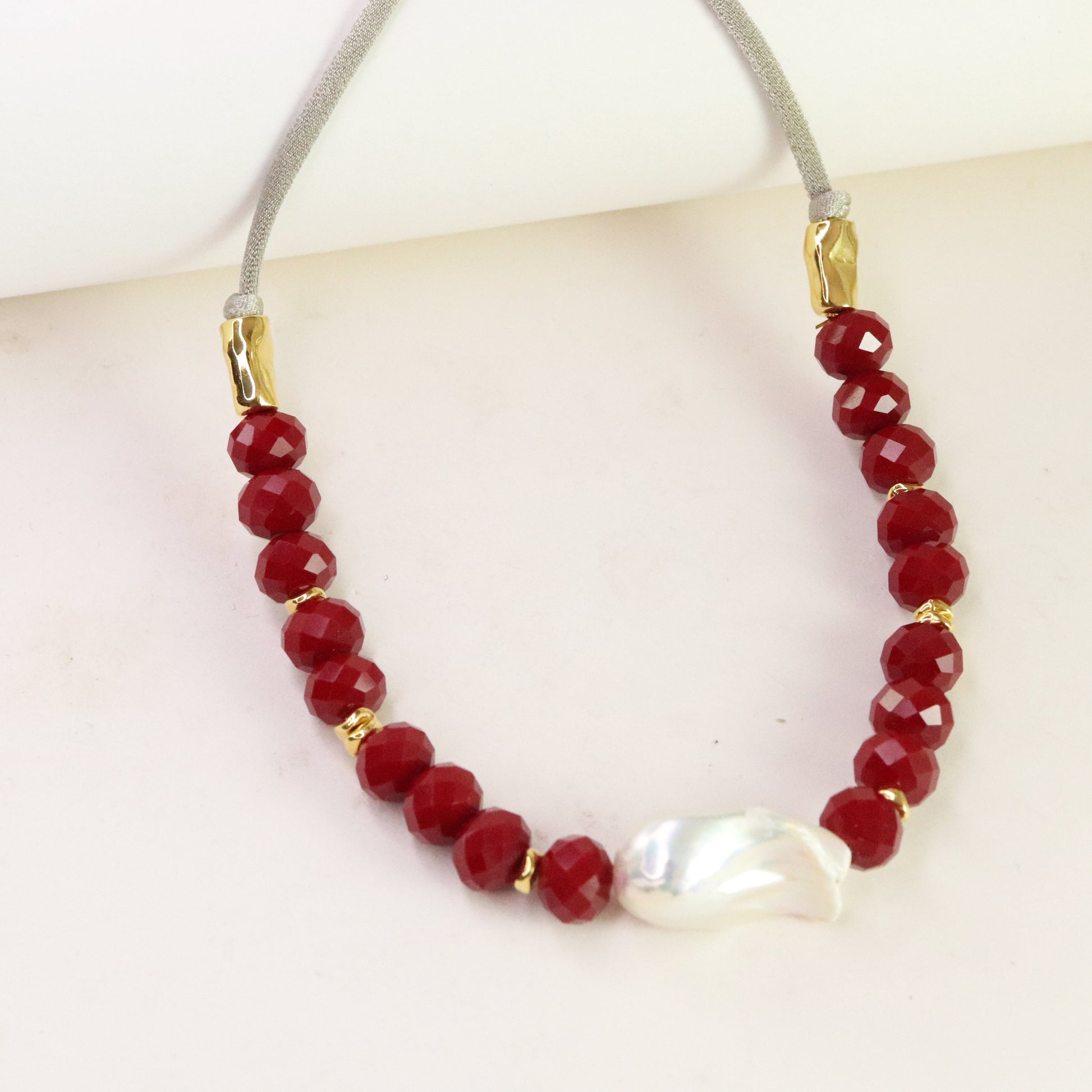 Collar de cuentas rojas facetadas y perla, con cadena gris y detalles en dorado. Estilo elegante y moderno.