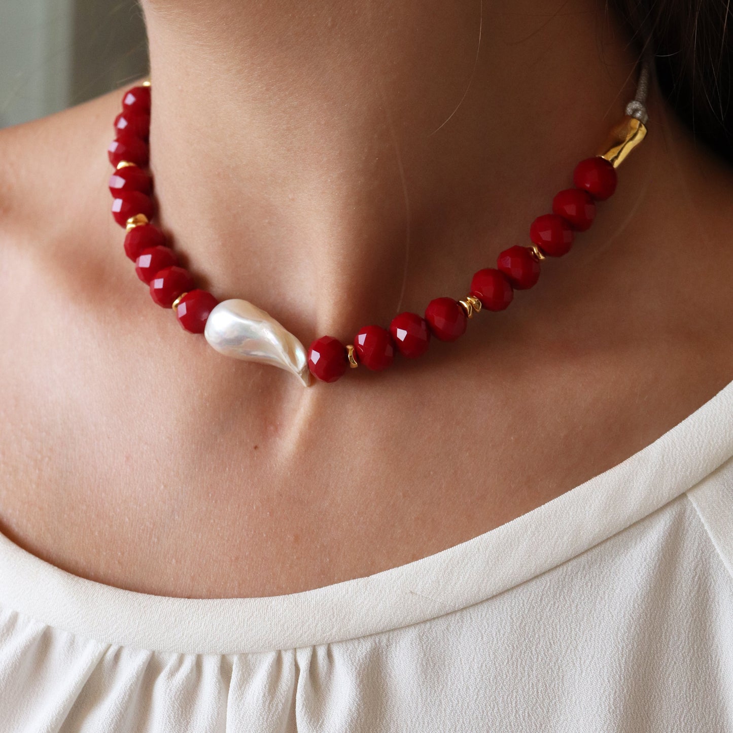 Collar de perlas rojas y doradas, con una perla blanca irregular en el centro, estilo elegante y moderno.