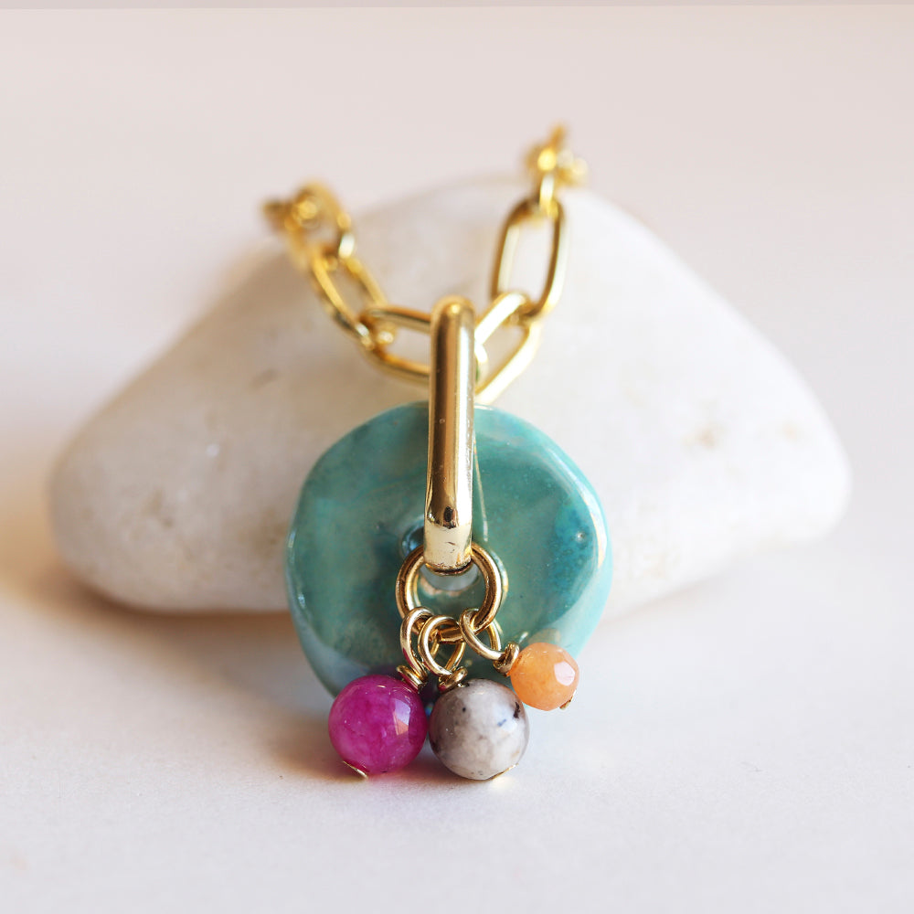 Collar de cadena dorada con colgante de cerámica turquesa y cuentas de gemas en rosa, blanco y naranja.