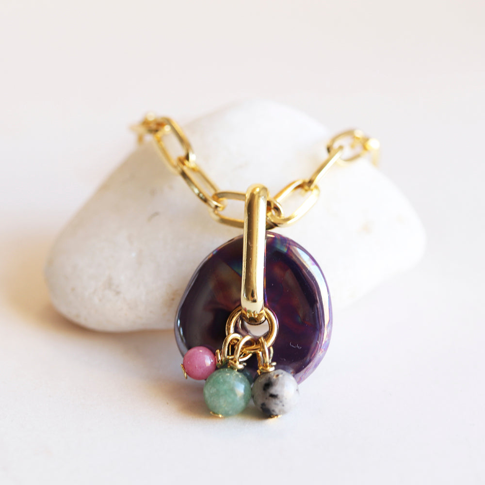 Collar de eslabones dorados con colgante de ópalo morado y piedras naturales en rosa, verde y gris.