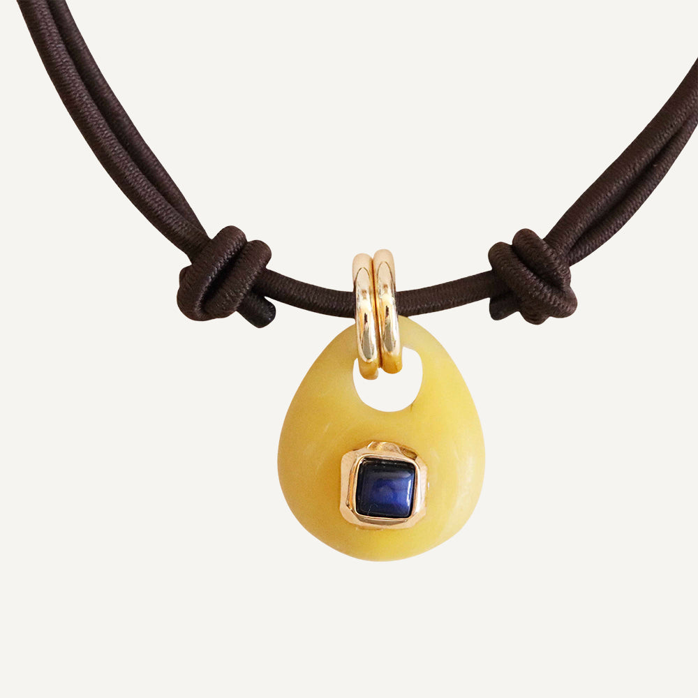 Collar de goma marrón con colgante amarillo y piedra azul, estilo moderno y artesanal.