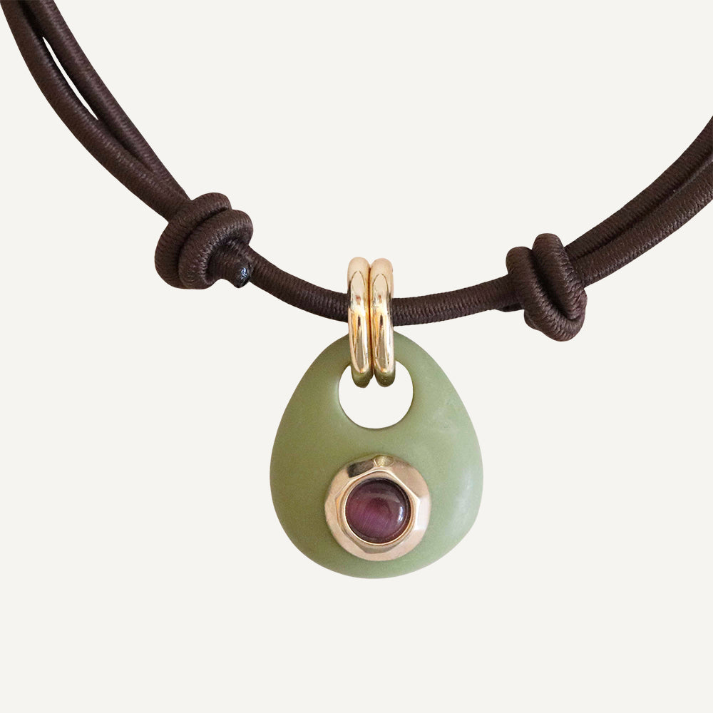 Collar de cordón marrón con colgante de jade verde y detalle dorado, adornado con una gema roja.