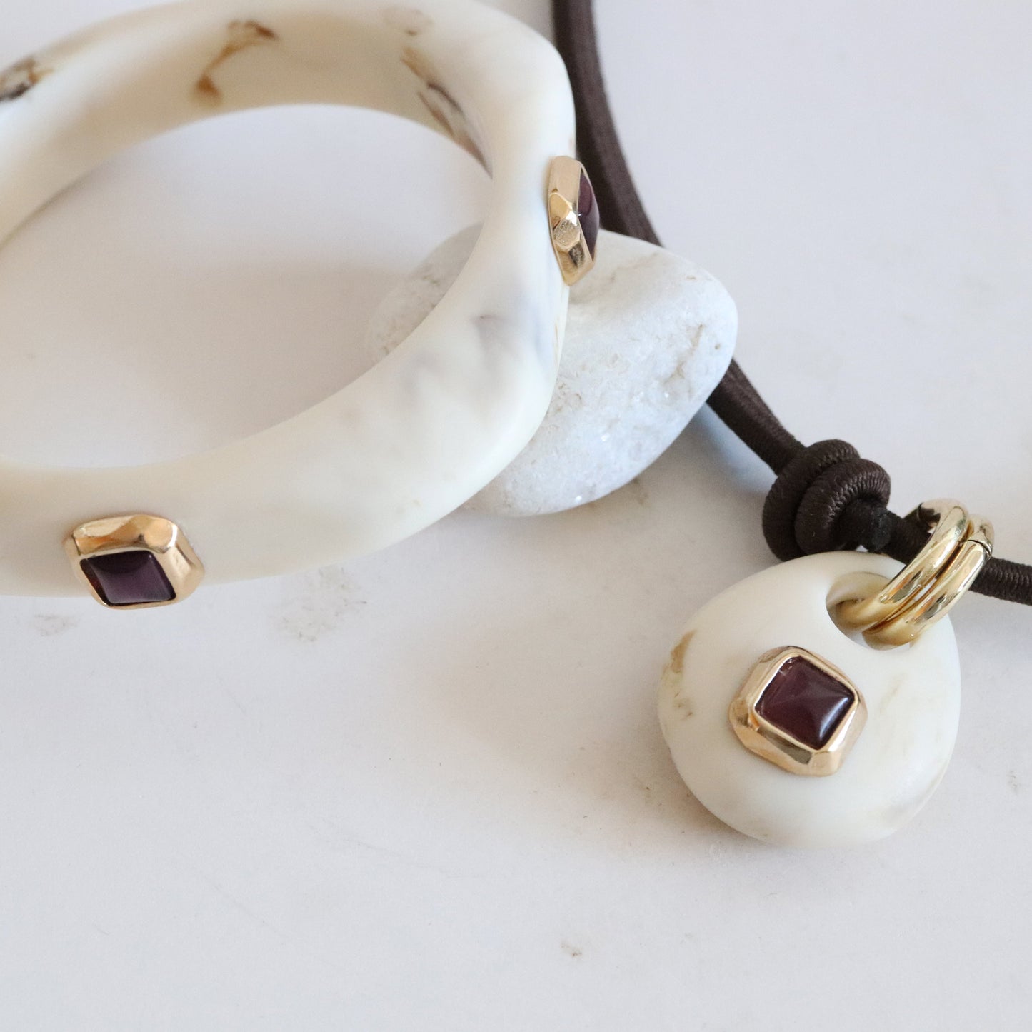 Pulsera y collar de resina blanca con gemas granate y detalles dorados, estilo moderno y elegante.