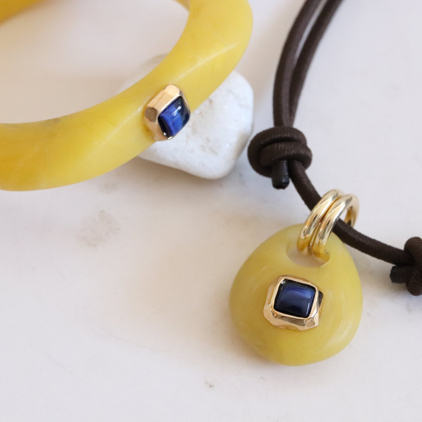 Joyería de resina amarilla con detalles en oro y zafiro azul, pulsera y colgante elegante y moderno.