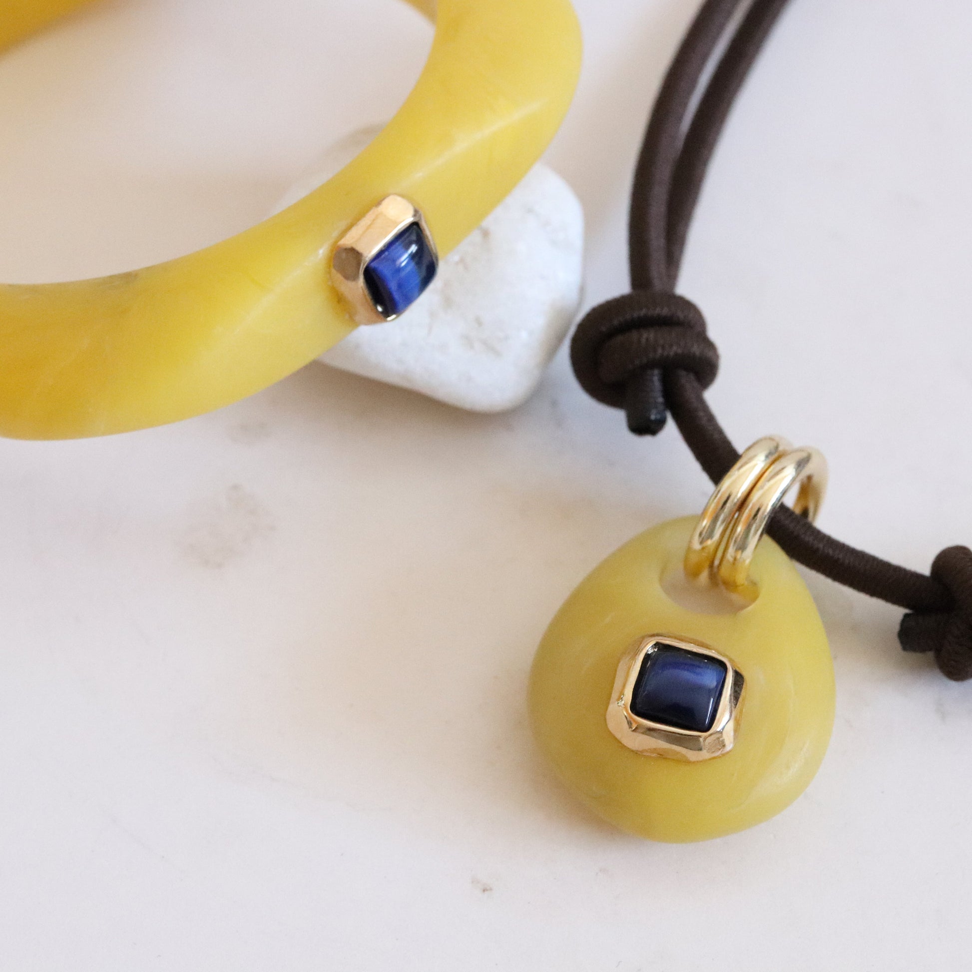Joyería de resina amarilla con detalles en oro y zafiro azul, pulsera y colgante elegante y moderno.