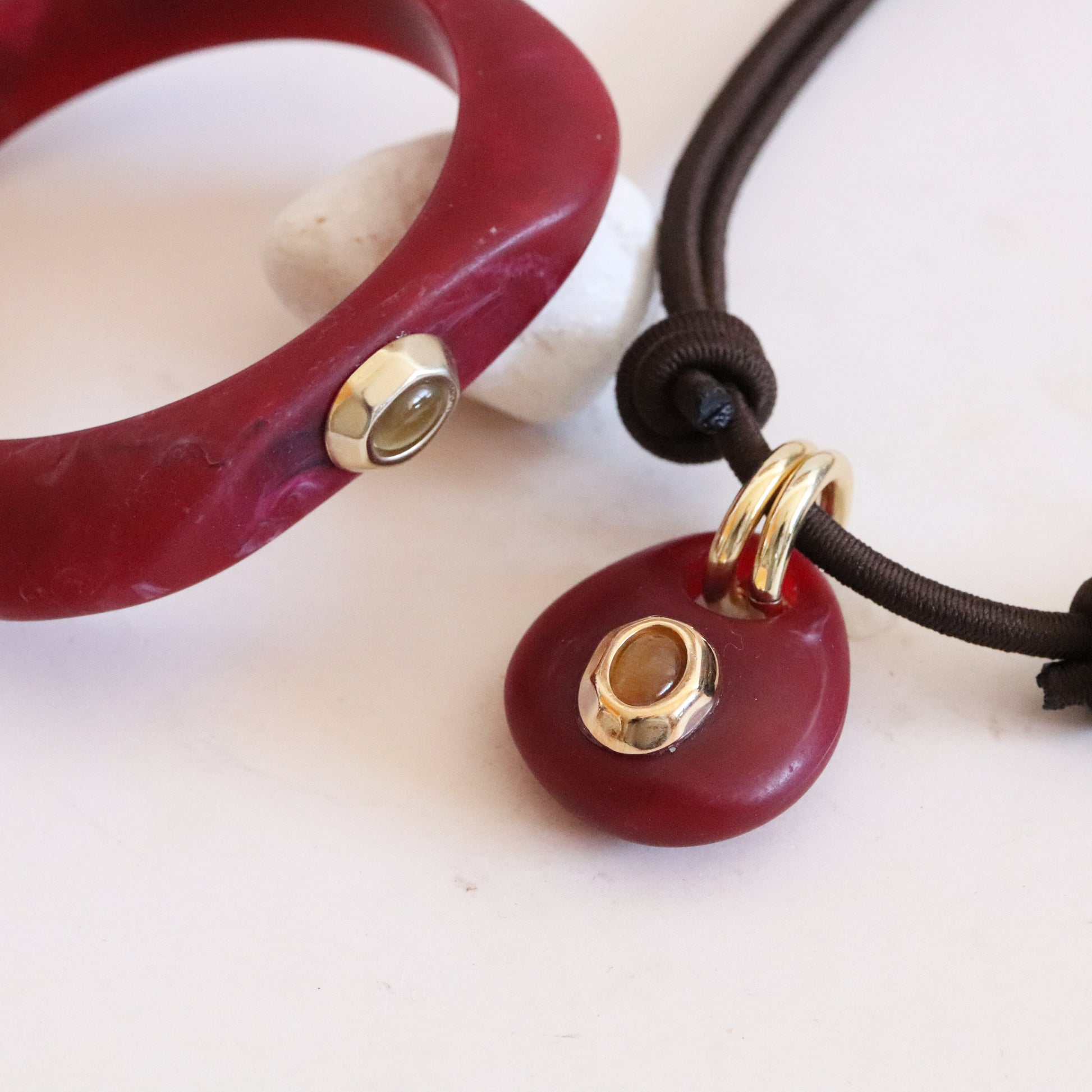 Pulsera y collar de cerámica roja con detalles en dorado y cordón marrón, estilo moderno y elegante.