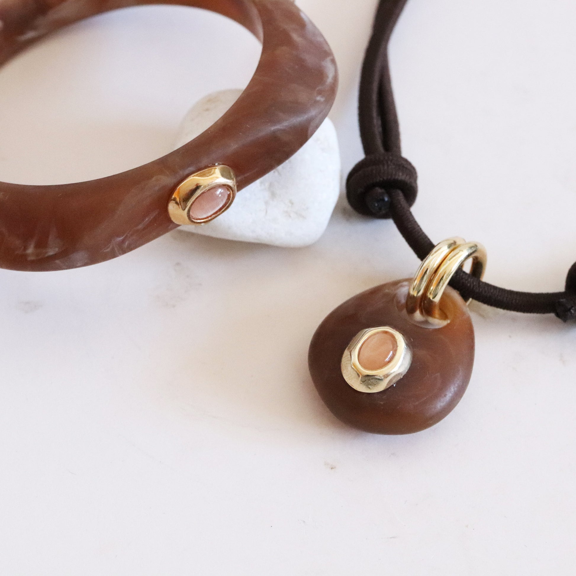 Brazalete marrón de resina y collar con colgante marrón y dorado, estilo moderno y minimalista.