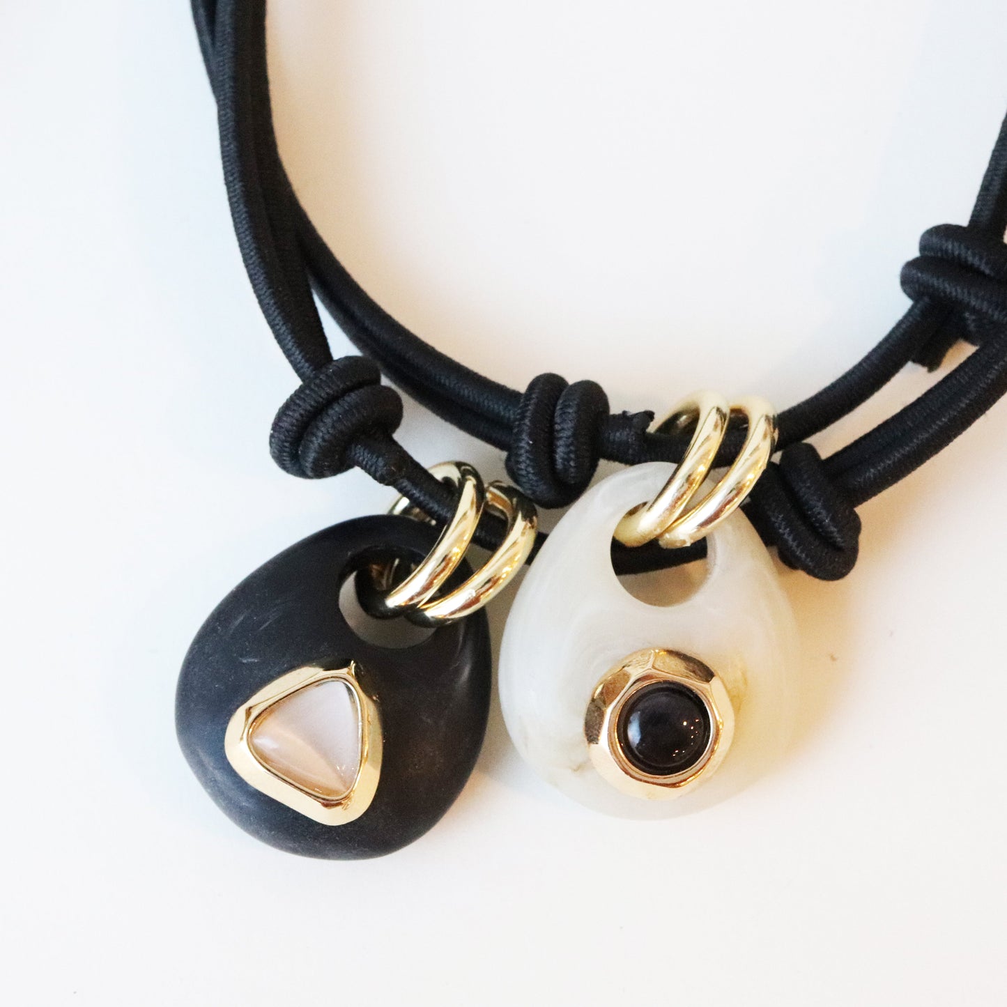 Collar de cordón negro con colgantes de resina negra y blanca, detalles dorados y piedras en forma de gota.
