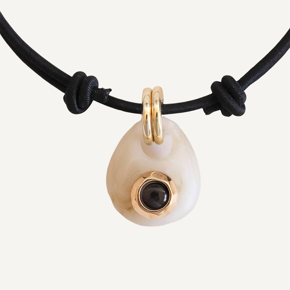 Collar de goma negra con colgante de piedra blanca y detalle dorado con gema negra en el centro.