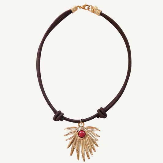 Collar de cuero marrón con colgante dorado en forma de ala y piedra roja, estilo bohemio.