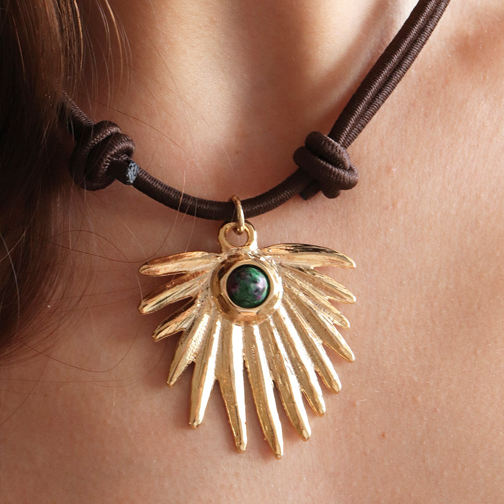 Collar de plata dorada con colgante en forma de ala y piedra verde, sobre cordón marrón.