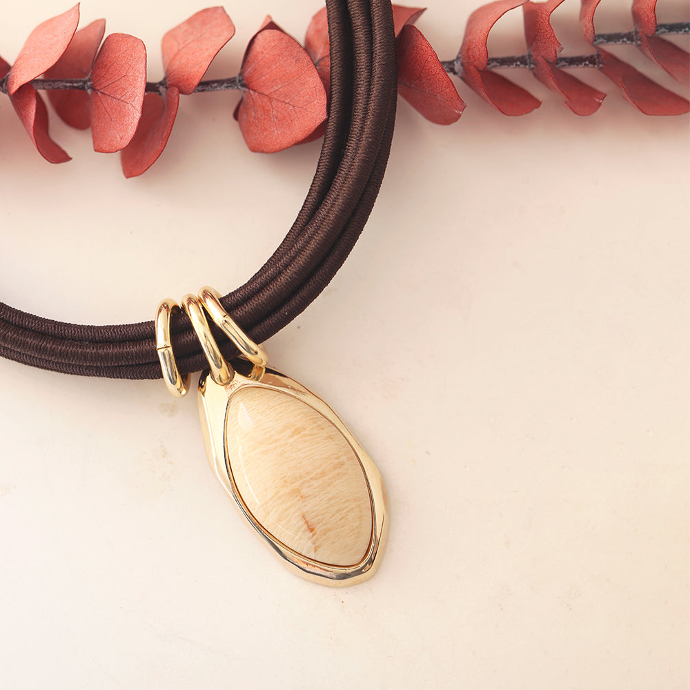 Collar de cordón marrón con colgante ovalado en oro y concha, estilo elegante y moderno.
