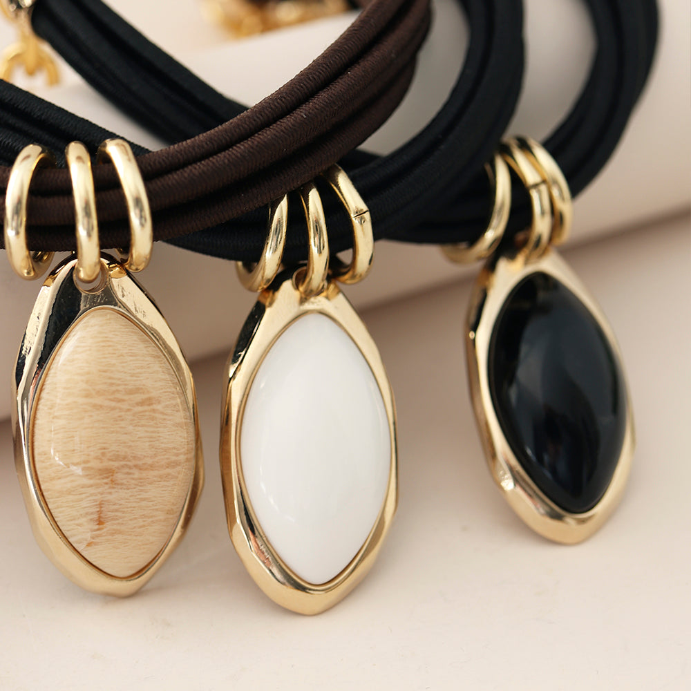 Collares con colgantes ovalados dorados y piedras en tonos beige, blanco y negro, con cadena de tela negra y marrón.