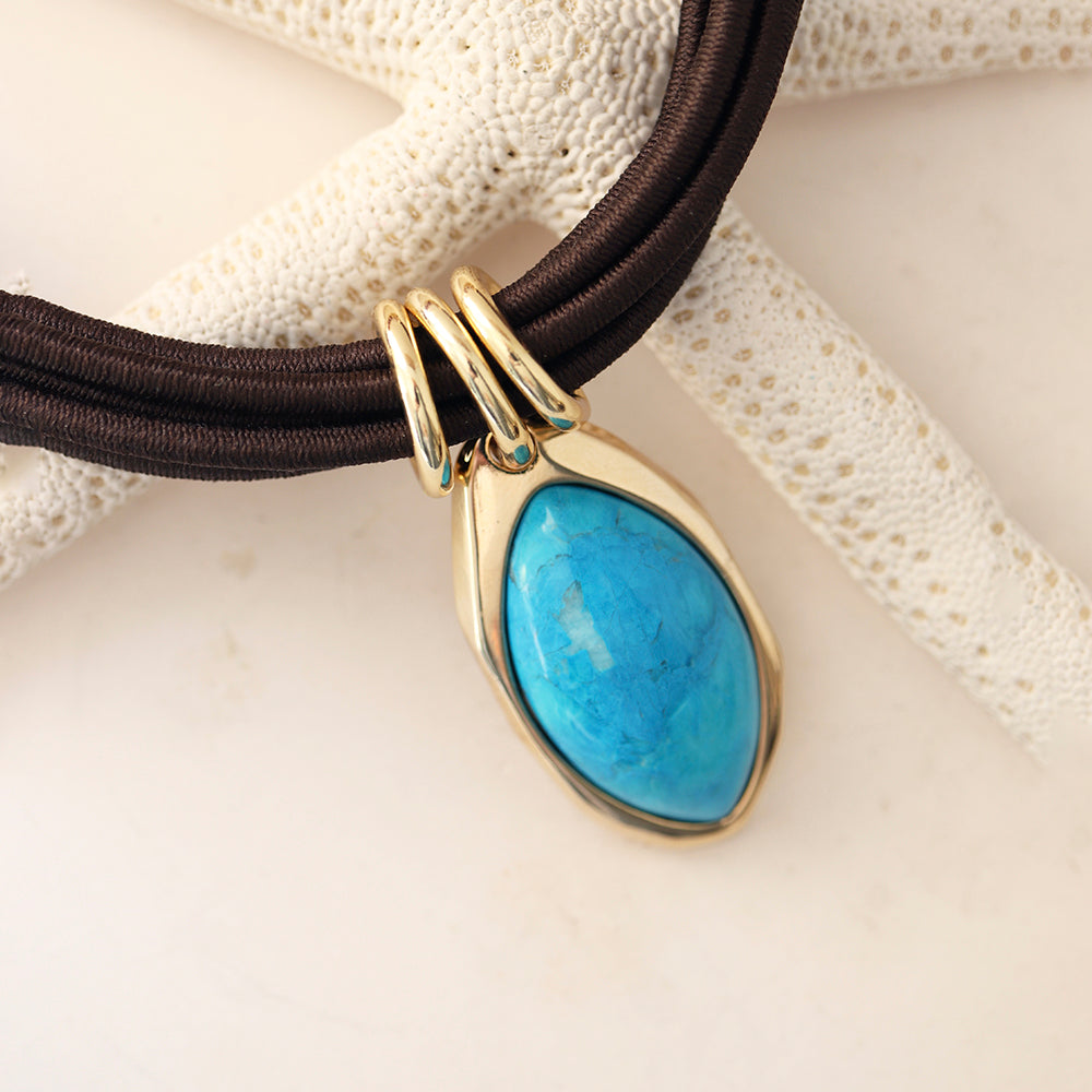 Collar con piedra turquesa y colgante dorado sobre cordón marrón, estilo elegante y moderno.