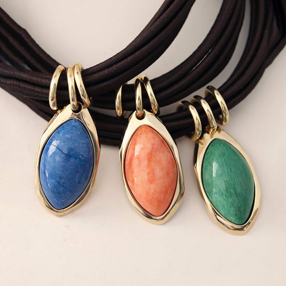Collares con colgantes de gemstone azul, naranja y verde con marco dorado sobre cadena marrón.