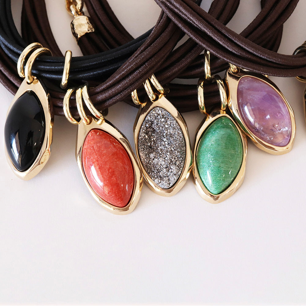 Collares de cuero marrón con colgantes de piedras preciosas en tonos negro, coral, verde, y morado.