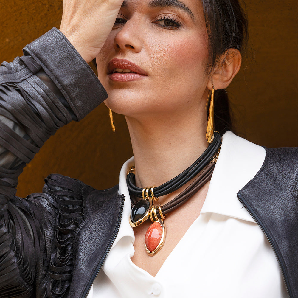 Mujer con collar de cuero negro y piedras preciosas, blusa blanca y chaqueta de cuero negro con detalles de flecos.