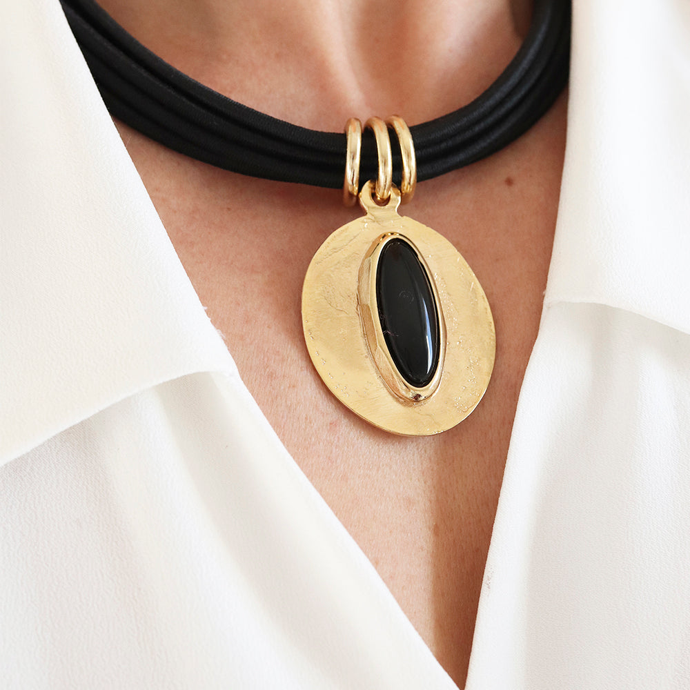 Collar de cuero negro con colgante dorado y piedra negra, estilo elegante y moderno.