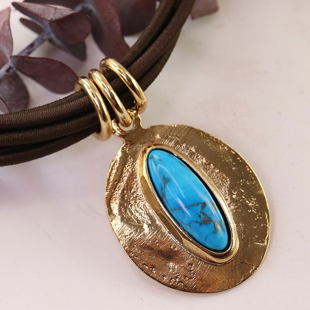 Collar de cuero marrón con colgante ovalado de metal dorado y piedra turquesa. Estilo bohemio y moderno.