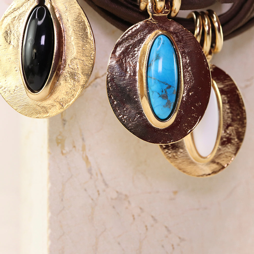 Pendientes de metal dorado con piedras turquesa, negra y blanca en diseño ovalado y elegante.