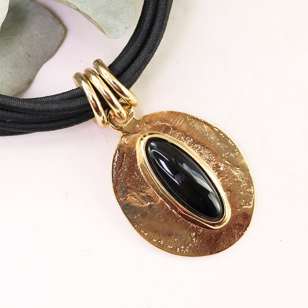 Collar de cuero negro con colgante ovalado dorado y piedra negra, estilo bohemio y elegante.