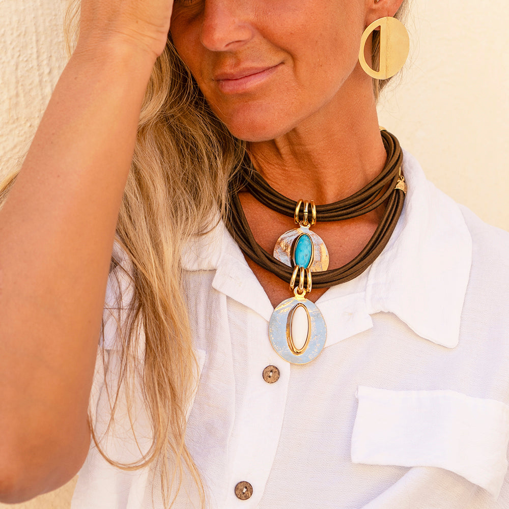 Collar de cuero marrón con apliques dorados y piedras turquesas, estilo bohemio, acompañado de pendientes dorados.