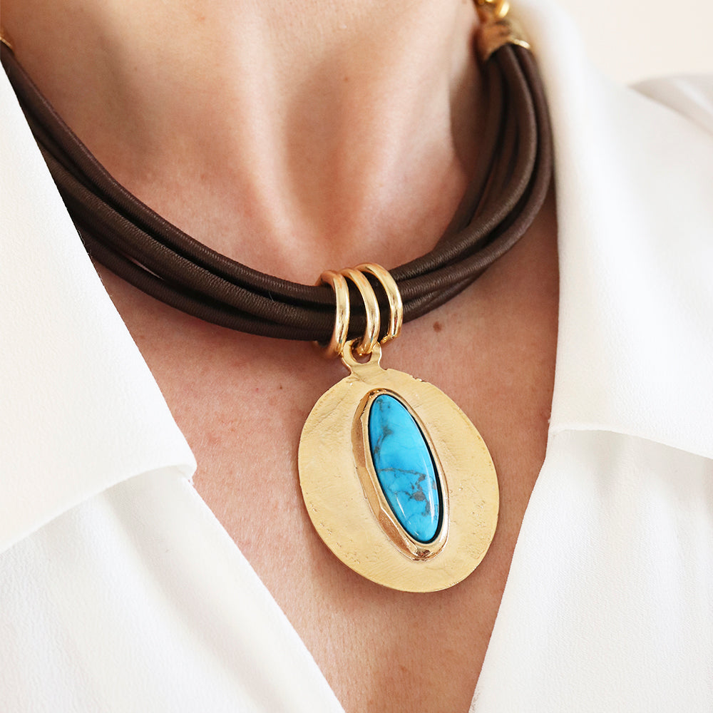 Collar de cuero marrón con medallón dorado y piedra turquesa, estilo moderno y elegante.