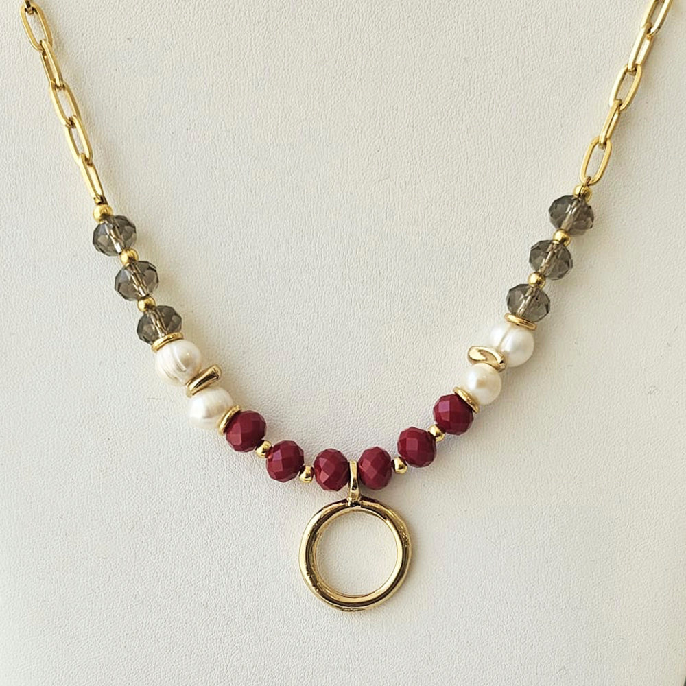Collar de perlas blancas, cuentas rojas y grises, con eslabones dorados y un colgante circular.