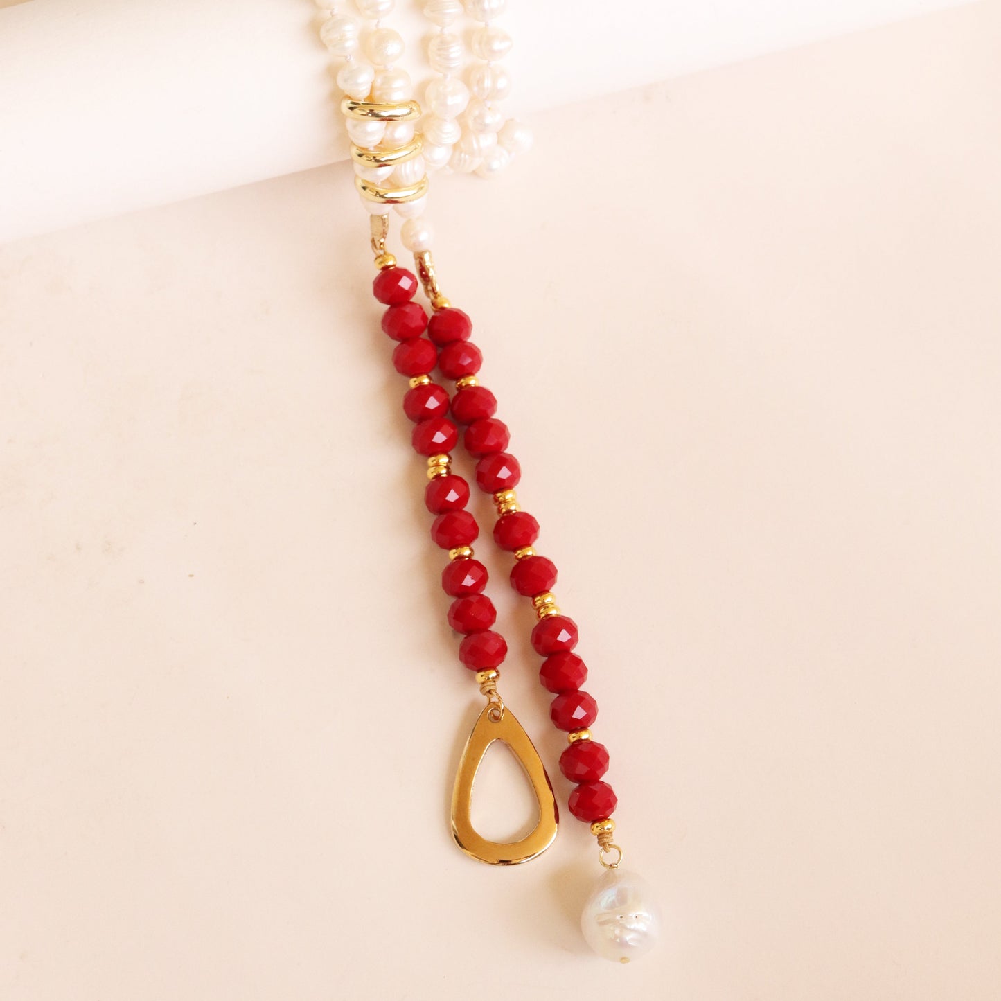Collar de perlas y piedras rojas con colgante dorado en forma de gota, estilo elegante y moderno.