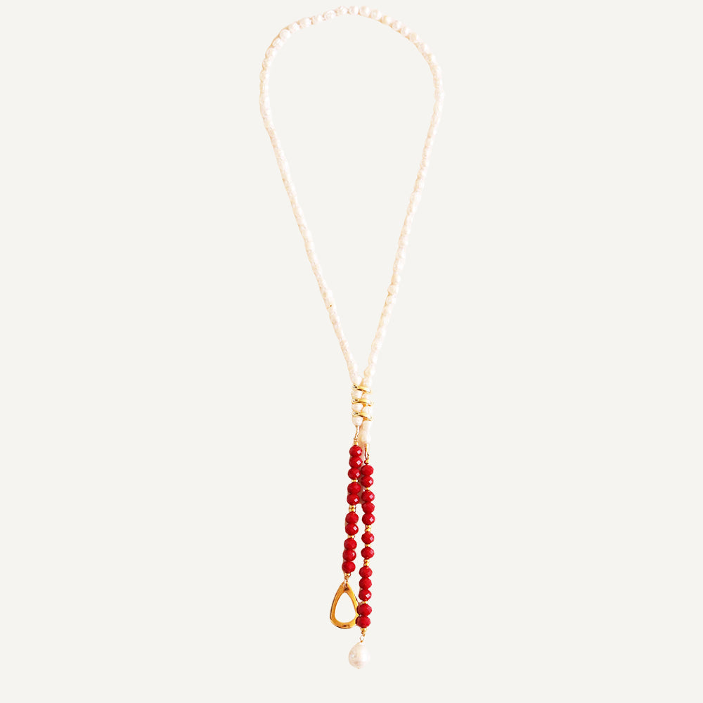 Collar largo de perlas blancas con cuentas rojas y detalle dorado, estilo bohemio y elegante.