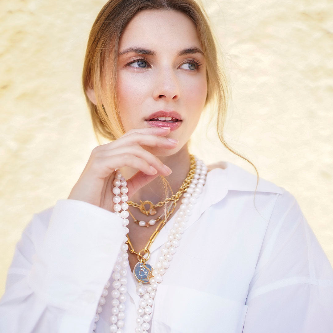 Collar de perlas y cadenas doradas, estilo elegante, sobre blusa blanca, toque moderno y sofisticado.