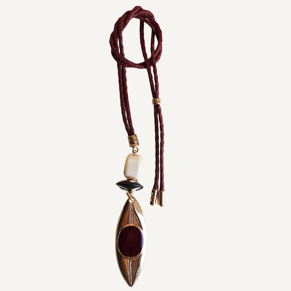 Collar largo de cuero burdeos con colgante ovalado dorado y piedras negras y rojas. Diseño moderno y bohemio.