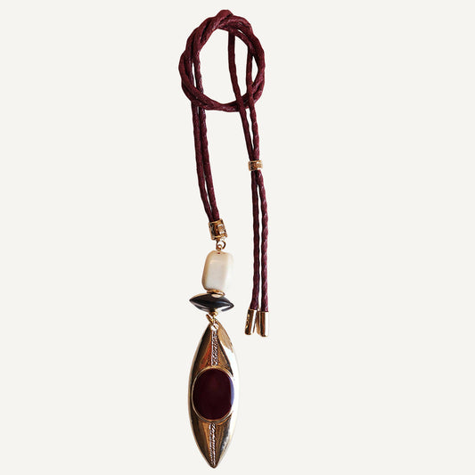 Collar largo de cuero burdeos con colgante ovalado dorado y piedras negras y rojas. Diseño moderno y bohemio.