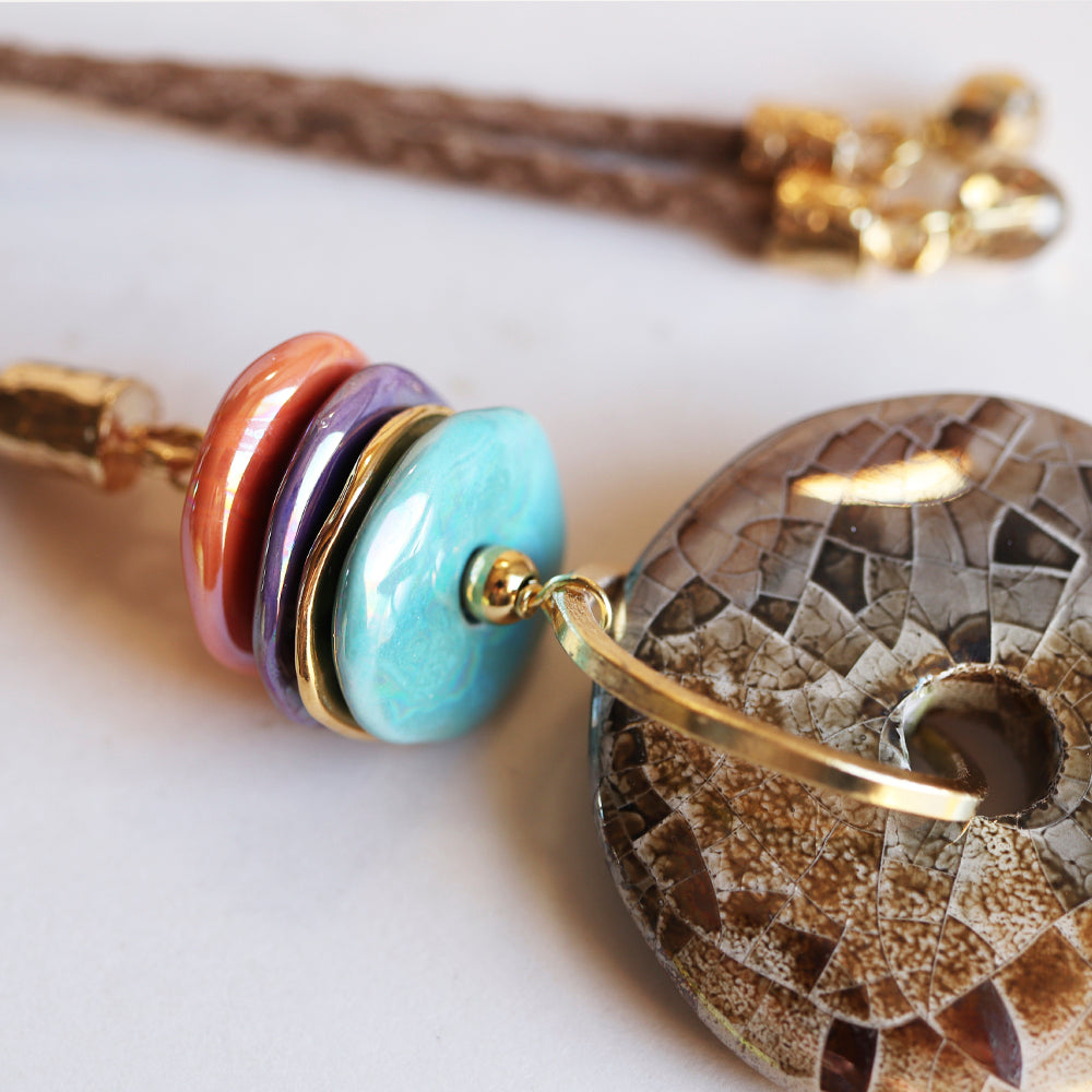 Pendiente bohemio de resina en tonos coral, lila y azul, con detalles dorados y un disco de piedra decorativa.