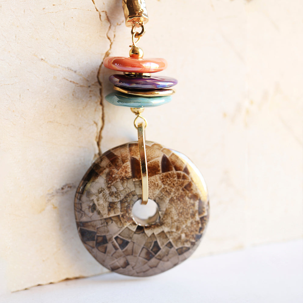 Pendiente de disco de piedra marrón con dijes de acrílico en tonos coral, morado y verde, estilo moderno y colorido.