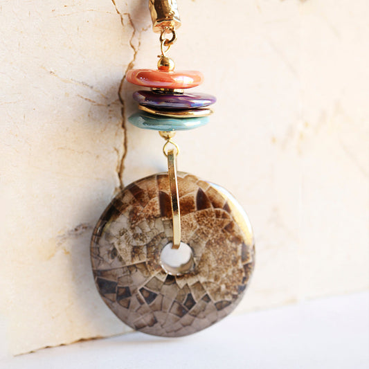 Pendiente de disco de piedra marrón con dijes de acrílico en tonos coral, morado y verde, estilo moderno y colorido.