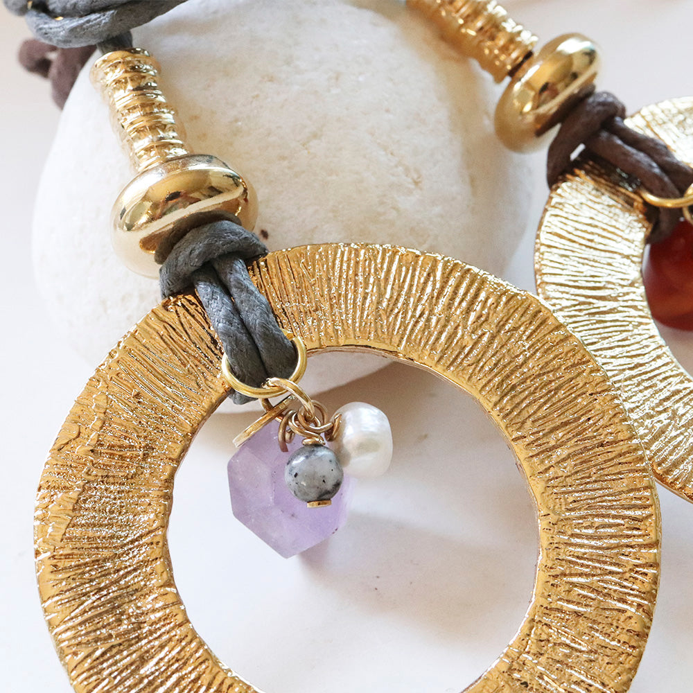 Aretes de metal dorado con acabados texturizados, detalles en amatista, perla y cuero gris. Estilo bohemio.
