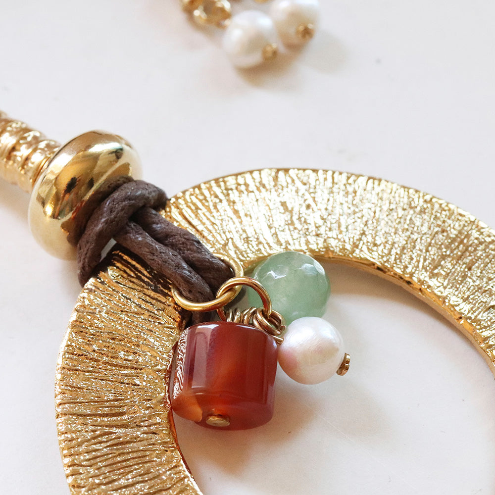 Collar artesanal con colgante dorado, piedras de ágata roja, perla blanca y jade verde, con detalles de cuero marrón.