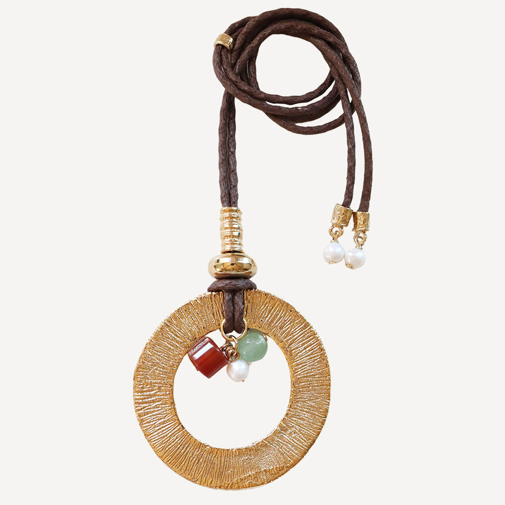 Collar de cuero marrón con colgante dorado, piedras de jade verde y ámbar, y perlas blancas.