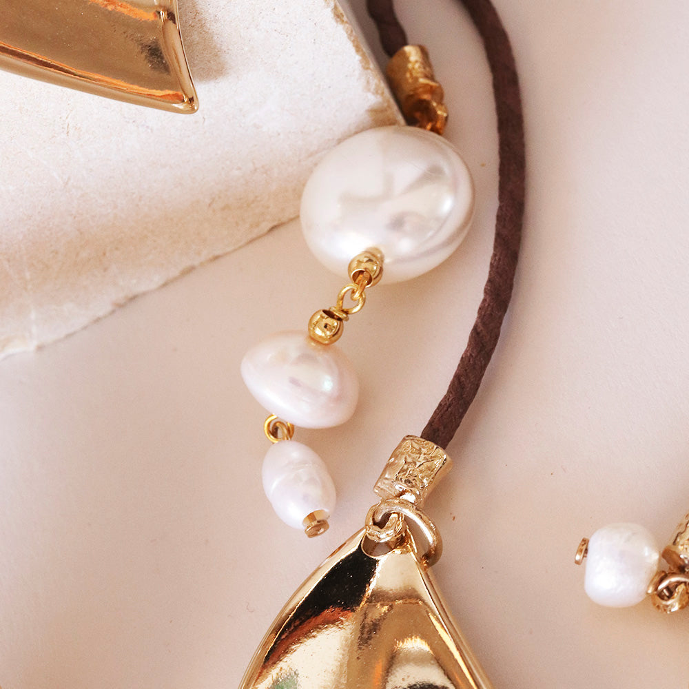 Collar de perlas blancas con detalles dorados y cordón marrón, estilo elegante y moderno.