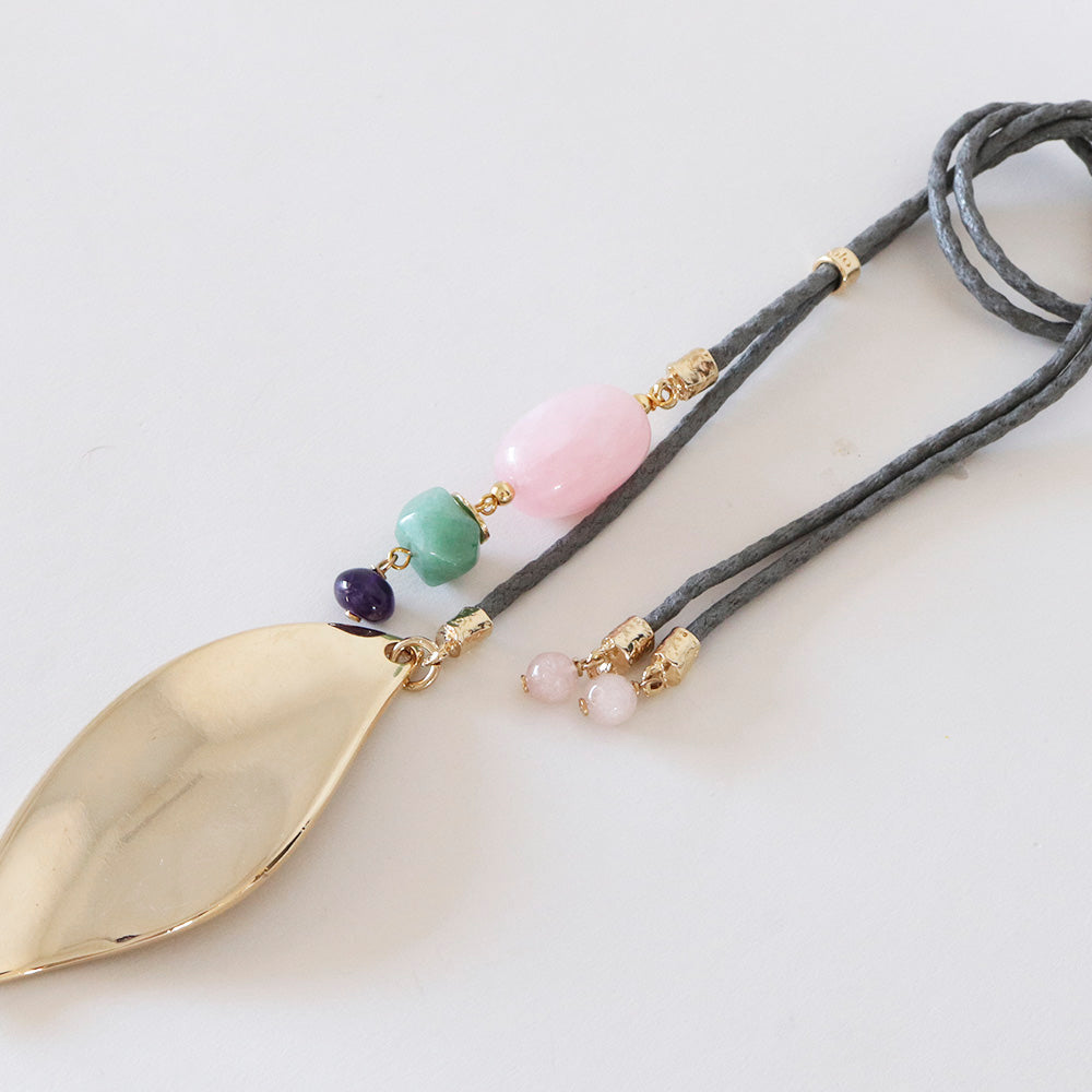 Collar de acero dorado con hoja, cuentas de jade verde, cuarzo rosa y cordón gris. Estilo bohemio y elegante.