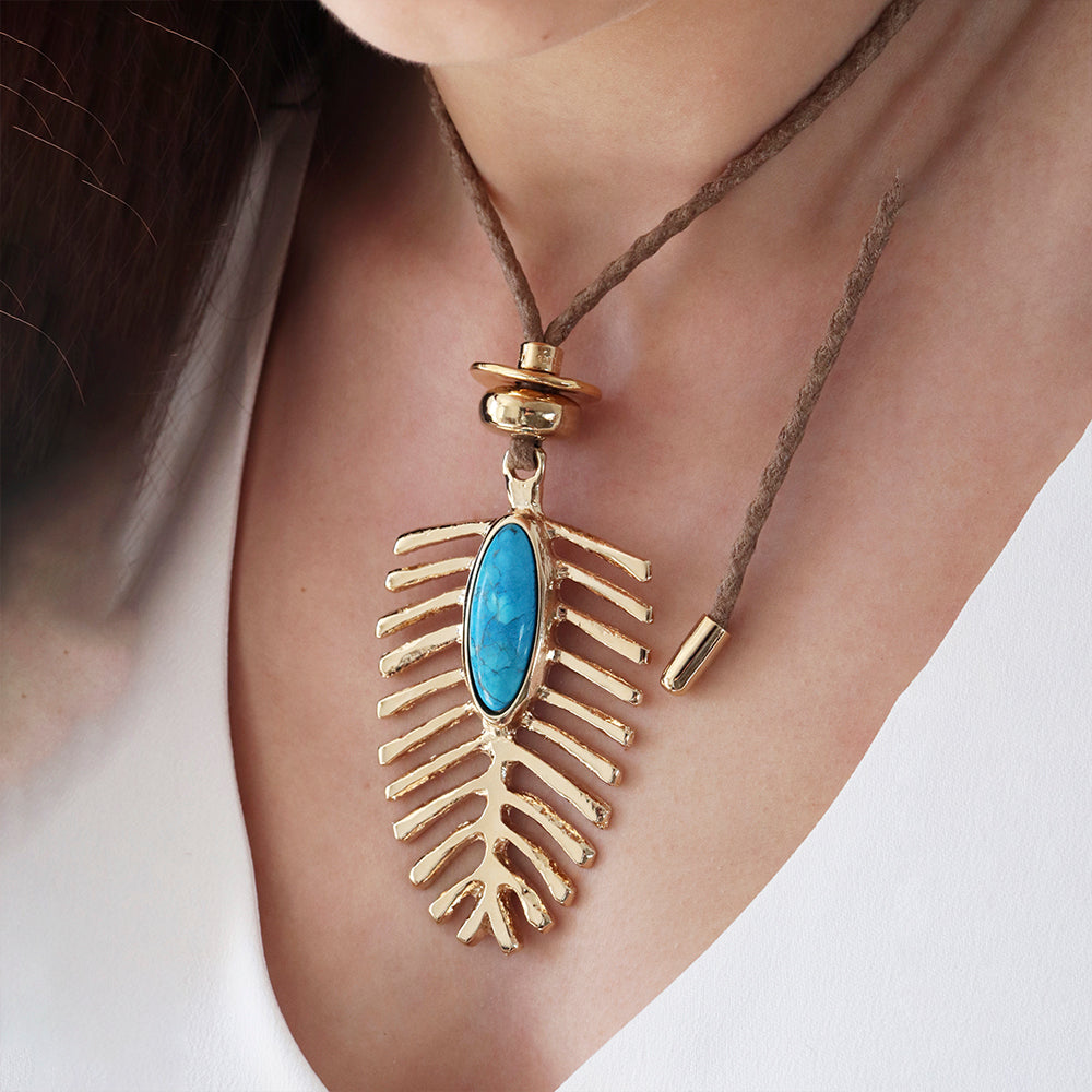 Collar bohemio con colgante dorado en forma de hoja y piedra azul, hecho de metal y cuerda natural.