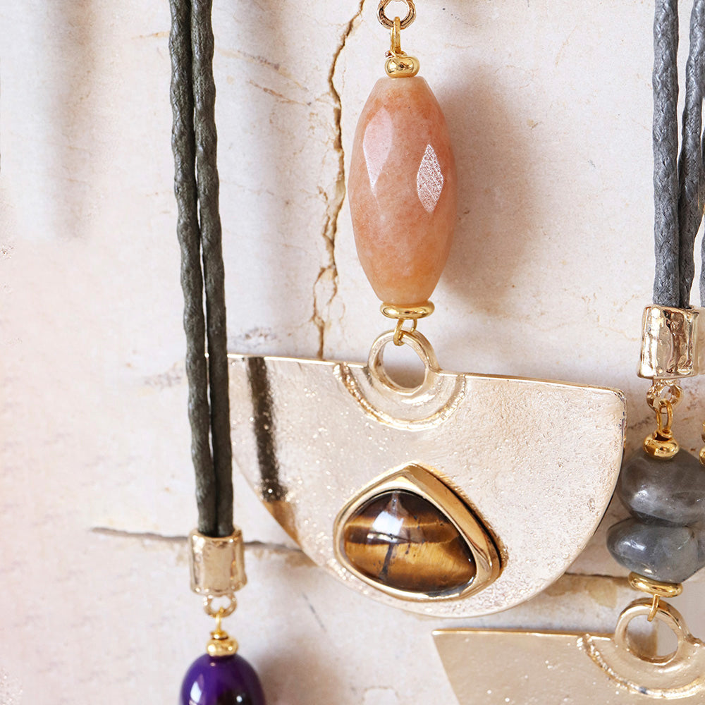 Collar largo de cuero negro con piedras semipreciosas en tonos dorado, naranja y púrpura, estilo bohemio elegante.