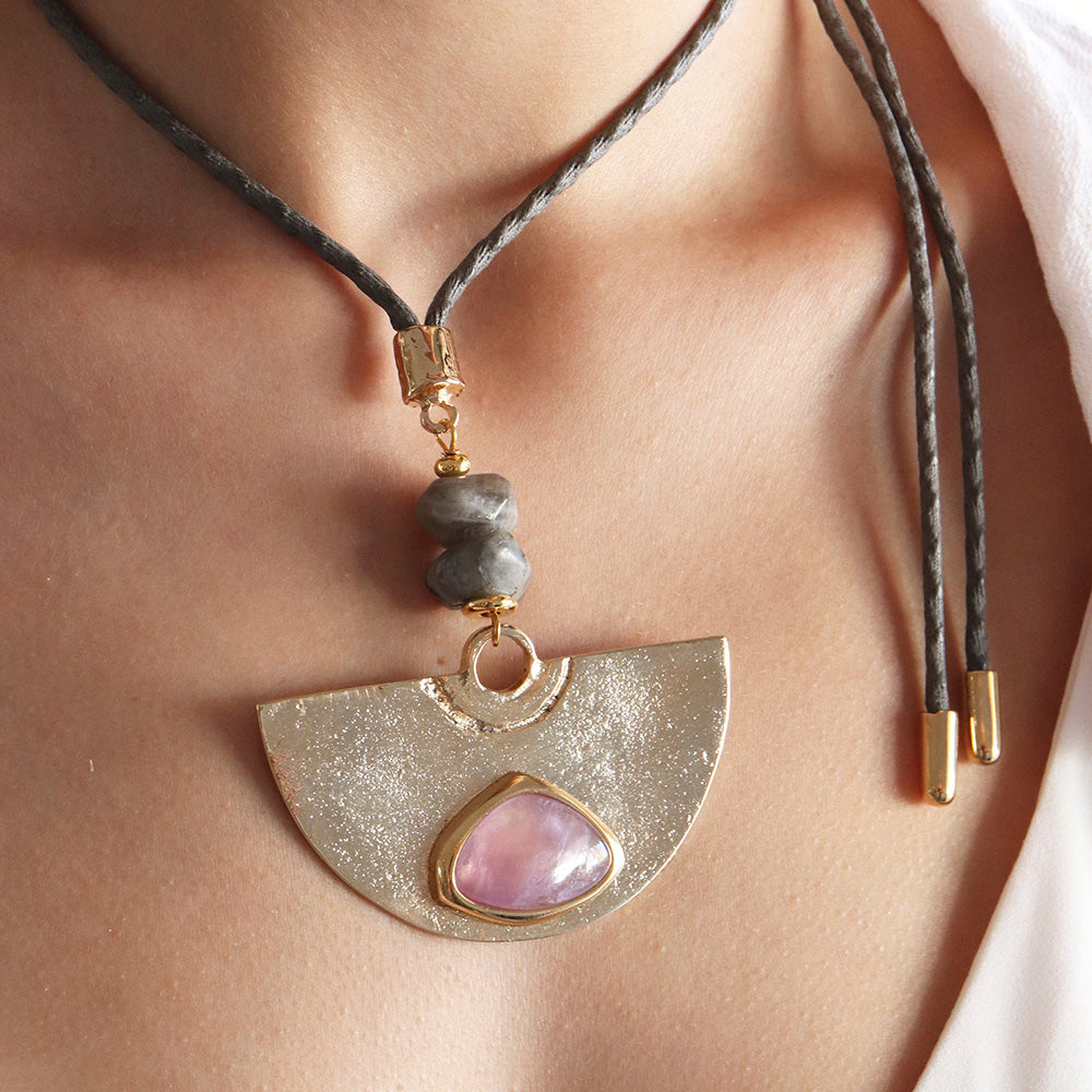 Collar artesanal con colgante dorado, gema rosa, y cuentas grises, estilo bohemio. Ideal para ocasiones especiales.
