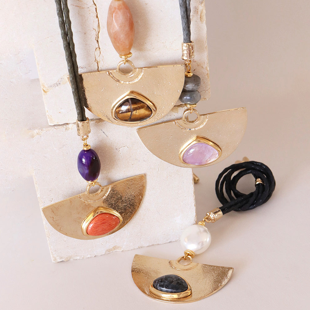 Collares de colgante dorado con piedras semi-preciosas en tonos rosa, morado, negro y naranja, sobre cordones de cuero.