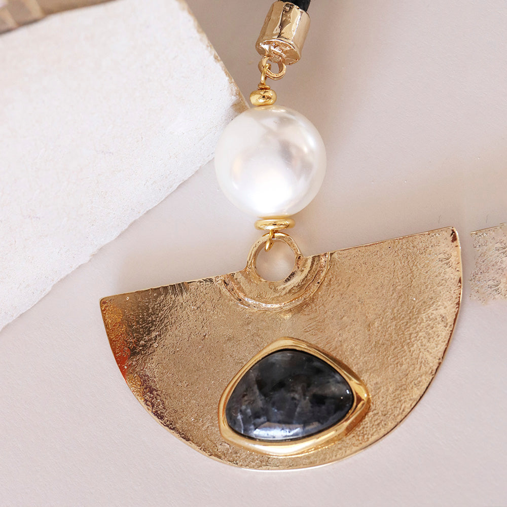 Pendiente dorado con piedra negra y perla blanca, diseño moderno y elegante en metal brillante.
