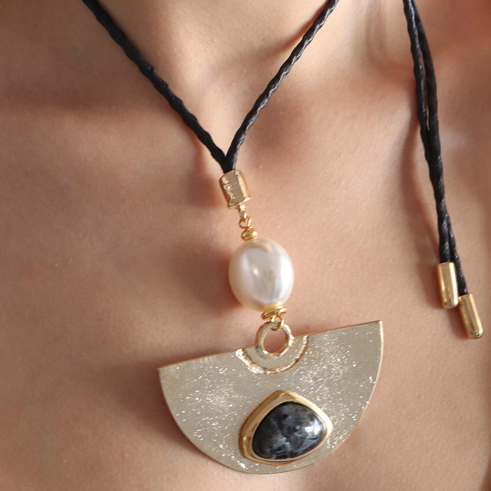 Collar de cuero negro con colgante semicircular dorado, piedra negra y perla blanca. Estilo bohemio y elegante.
