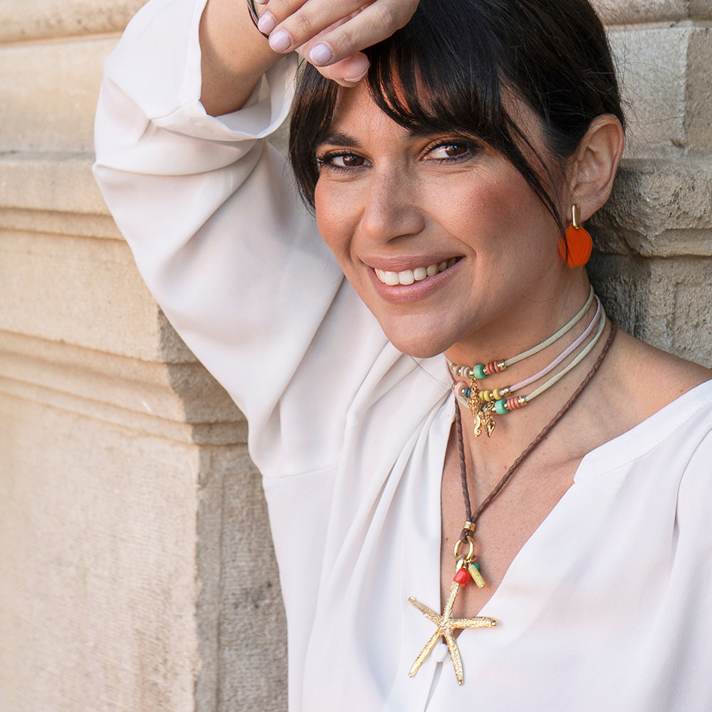 Collar de estrella de mar en tonos dorados y coral, con cordones de cuero y cuentas coloridas, estilo boho-chic.