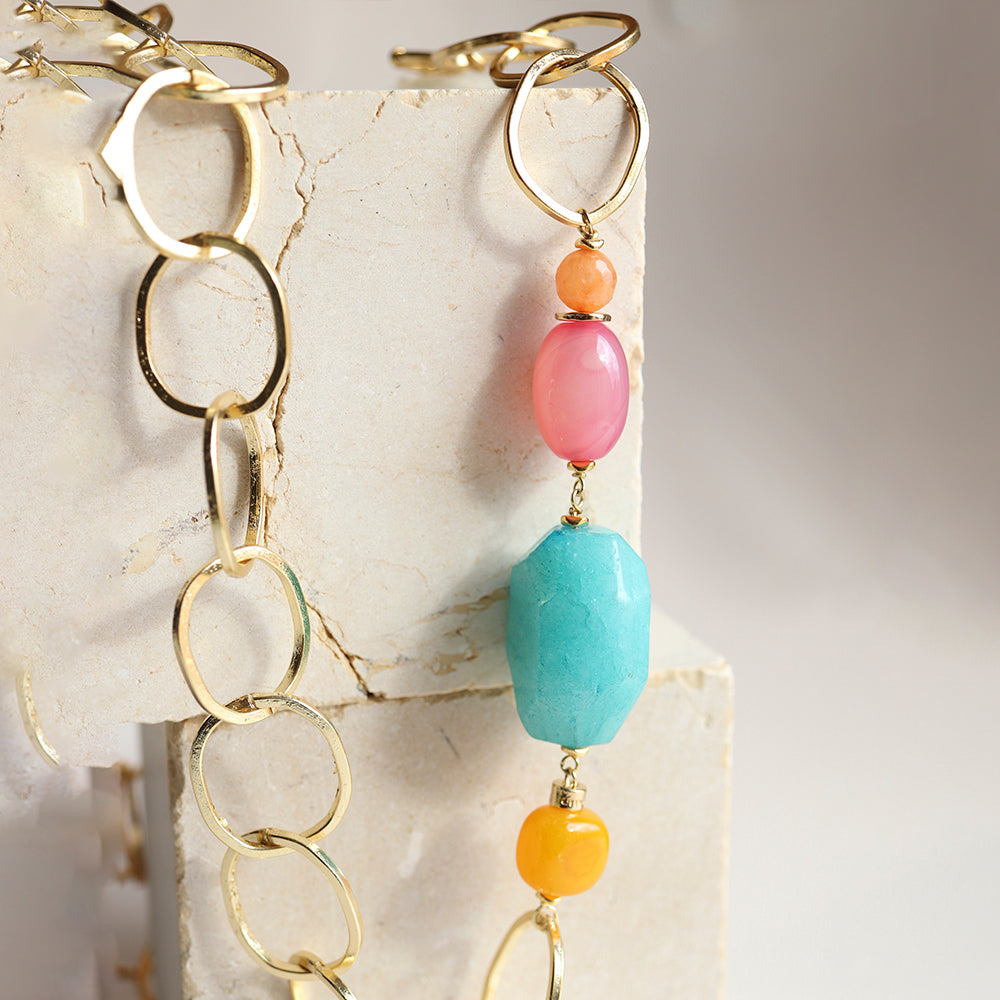 Collar de eslabones dorados con piedras turquesas, rosas y naranjas, estilo moderno y vibrante.
