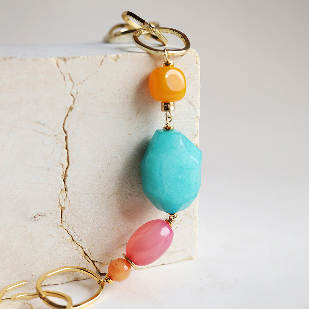 Collar de piedras preciosas en tonos azul, naranja y rosa, con detalles en dorado, estilo bohemio y moderno.